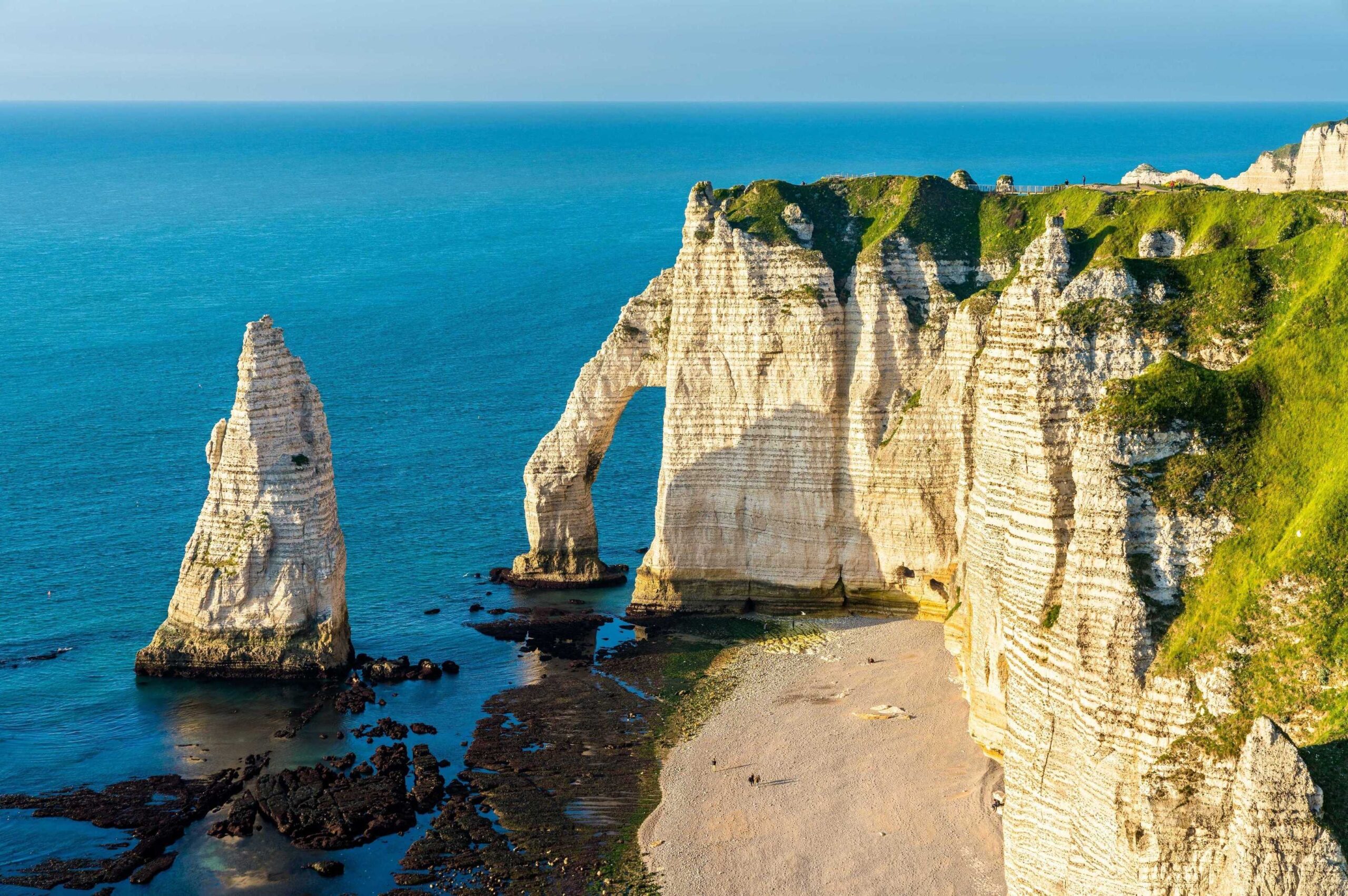 The Falaise d'Aval cliffs in Étretat in Normandy against a clear blue sea on a sunny day.