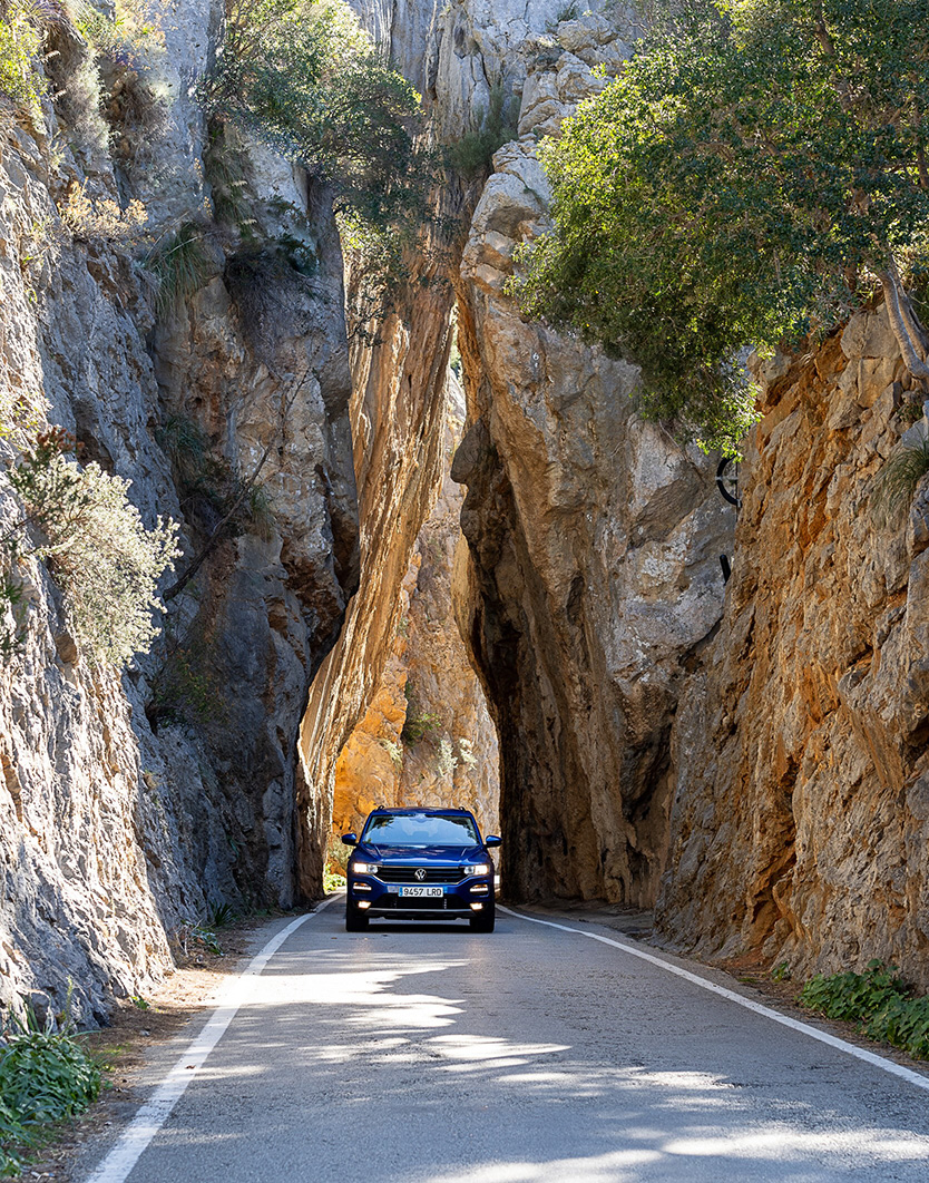 A car drives through a narrow mountain pass between towering cliffs. 