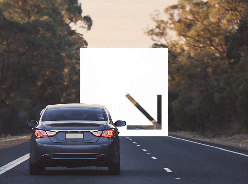 Car driving on an open road at sunset surrounded by trees.