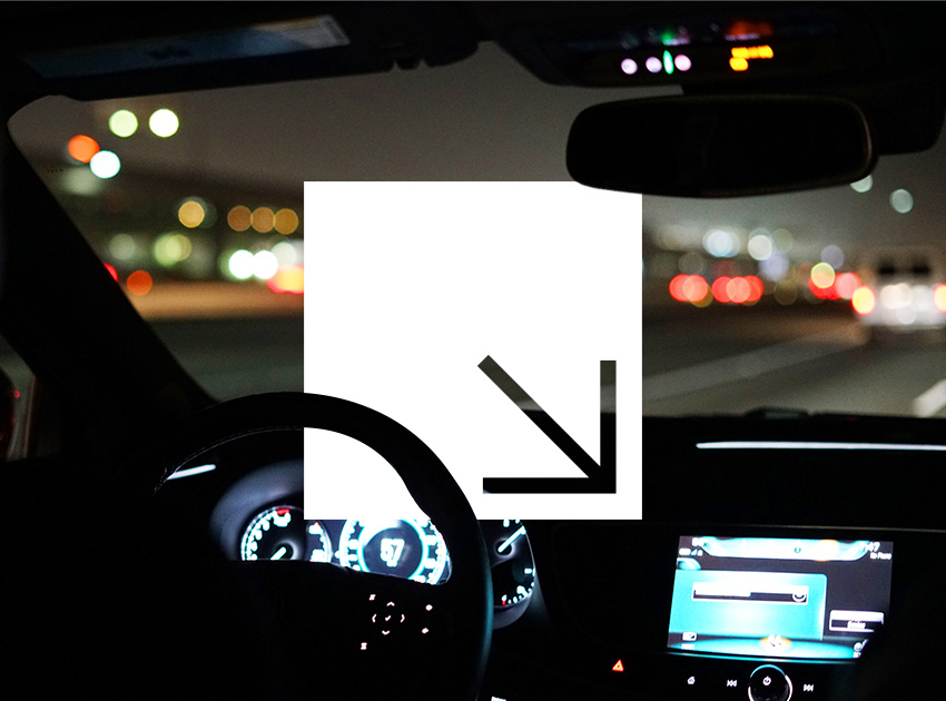 Driver’s view of a car interior and dashboard while driving at night with blurred city lights.
