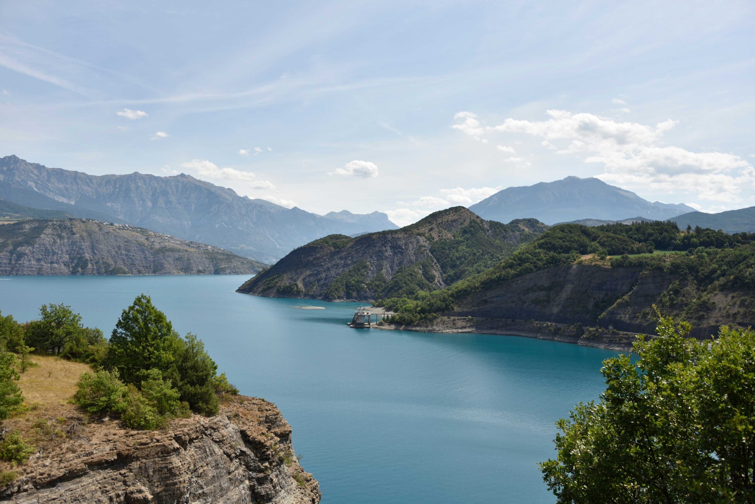 Lac de Serre-Ponçon under a clear sky reflecting light and surrounded by distant land.