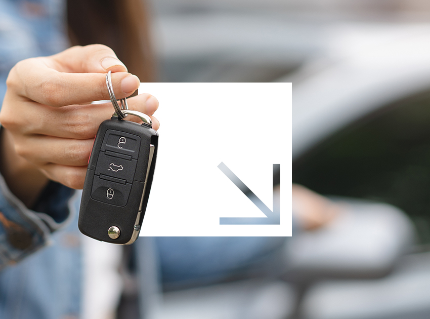 A person holds a car key fob prominently with a blurred car in the background.